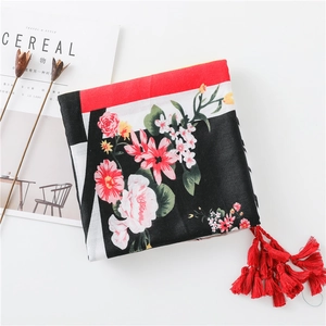 Détail d'une écharpe en coton et lin à fleurs avec de longs pompons rouges et imprimés