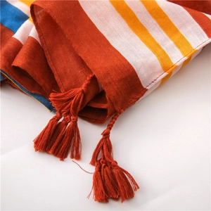 Detail of colorful striped scarf featuring breathable fabric texture and red fringe tassels