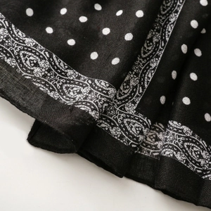 Detail of black scarf featuring white polka dots and intricate paisley floral border