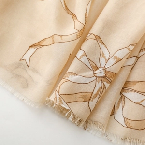 Détail d'une écharpe en lin beige clair avec motif nœud et bords effilochés
