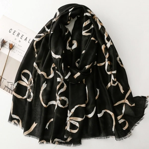 Détail d'une écharpe noire avec motifs de rubans et bords effilochés sur fond blanc