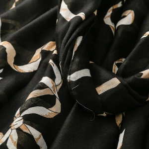 Détail macro d'une écharpe en coton et lin avec des motifs de rubans crème sur fond noir