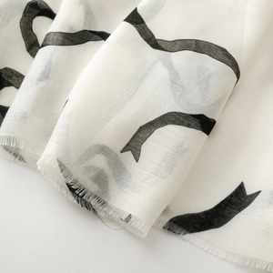 Détail d'une écharpe en coton et lin blanc avec ruban noir et fines franges aux bords