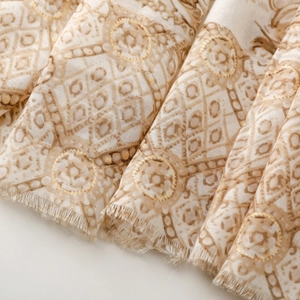 Détail du motif géométrique doré sur une écharpe crème en coton et lin avec des franges