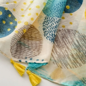 Détail d'un châle en coton aux imprimés abstraits bleus et jaunes avec des pompons colorés