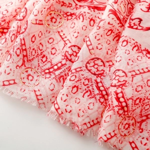 Détail d'une écharpe en coton doux avec accents dorés et franges en rose et rouge