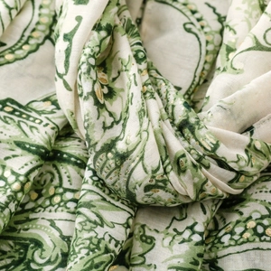 Détail macro d'une écharpe paisley avec pois dorés sur tissu respirant crème