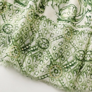 Détail macro d'une écharpe en coton vert avec motif paisley doré et des franges