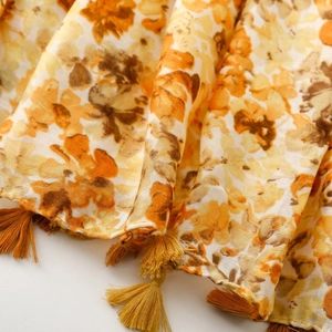 Macro detail of bohemian floral scarf with orange fringe and textured cotton-linen fabric