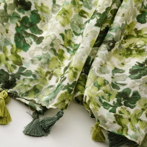 Detail of green floral linen scarf with intricate dual-tone tassels and soft texture