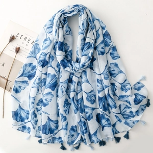 Detail of white scarf with blue gingko leaf print and delicate fringe tassels on cotton fabric