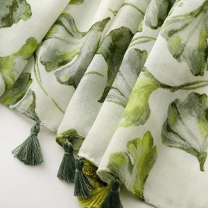 Detailed close-up of breathable fabric scarf with green ginkgo leaves and tassel fringe