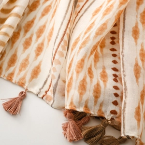 Detail of soft cotton scarf with abstract orange patterns and delicate pink fringe tassels