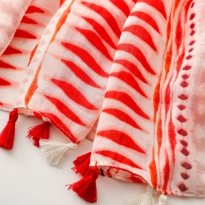 Detail of bohemian geometric pattern scarf featuring vibrant red and white tassels