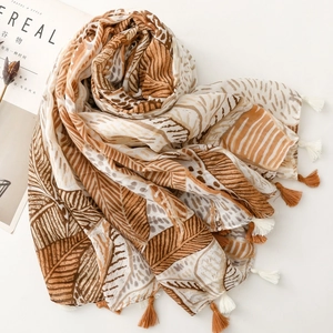 Detail of earthy tone scarf with leaf prints and decorative fringe tassels on soft fabric