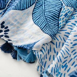 Detail of blue tropical leaf print scarf with two-tone tassel fringe and fabric texture