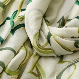 Detailed view of cream scarf featuring green leaf patterns and gold foil heart accents