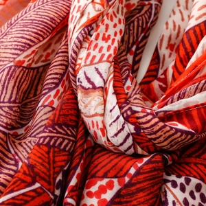 Detail of red and orange tropical leaf print on lightweight woven scarf fabric texture