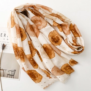Détail d'une écharpe crème douce avec accents dorés et motifs de points aquarelle bruns