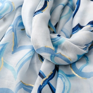 Detail of white cotton linen scarf featuring blue spiral patterns and gold foil edges