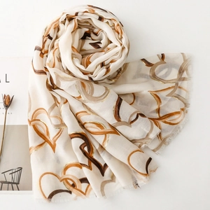 Macro detail of breathable cream scarf featuring gold foil heart patterns and fringed edges