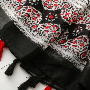 Détail d'une écharpe imprimé animal avec touches rouges et pompons sur fond blanc
