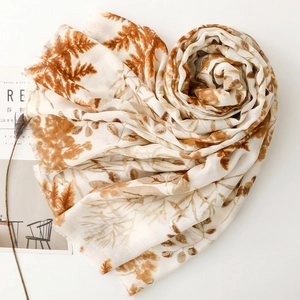 Detailed view of the linen-touch scarf featuring golden leafy print and fringe edges