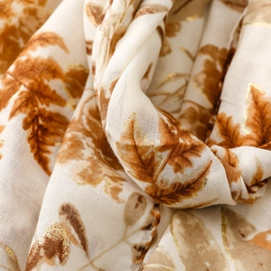 Detail of cotton linen scarf featuring gold foil autumn leaf patterns and textured fabric