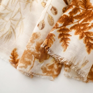 Close-up of beige cotton-linen scarf with golden brown leaf print and frayed edges