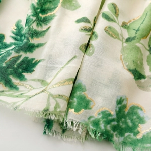 Detail of linen-feel scarf featuring lush green leaf prints and gold foil accents