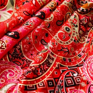 Detailed macro view of the paisley pattern and golden threads on a luxury red silk scarf