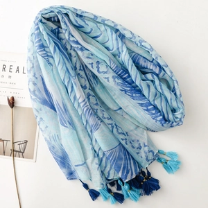 Flat lay of blue tropical leaf print scarf with tassels beside a lifestyle magazine