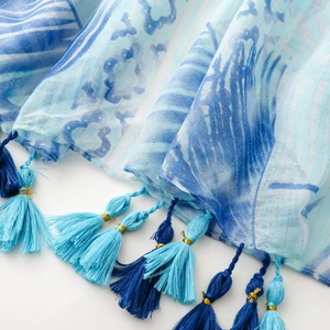 Detail of blue tropical floral scarf with gold lurex threads and multicolored tassels