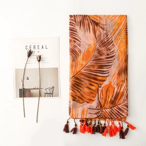 Close-up of tropical palm leaf print and fringe tassels on lightweight orange shawl scarf