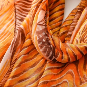 Detail of tropical scarf featuring golden threads and orange zebra stripe patterns