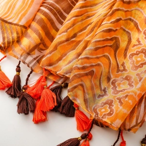Close-up of bohemian silk scarf with gold thread embroidery and orange tassel details