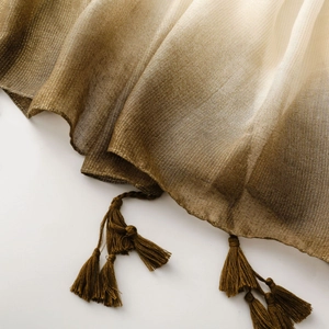 Detail of gradient bronze to cream shawl featuring sparkling metallic yarn and fringe tassels
