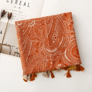 Close-up of orange bohemian paisley scarf with decorative fringe on a minimalist background