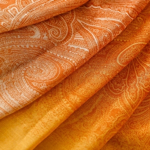 Close-up of bohemian paisley shawl fabric with orange gradient texture and fine tassels
