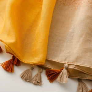 Close-up of bohemian scarf fabric showing yellow and beige linen texture with tassels