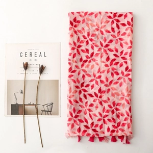 Pink scarf with red leaf patterns and fringes, styled in a minimalist setting