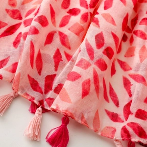 Close-up of pink shawl with geometric prints and fringe tassels on a textured fabric