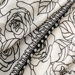 Detail of soft white scarf featuring black line-art rose prints and elegant ribbon border