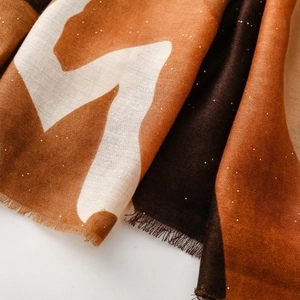 Détail des motifs géométriques avec paillettes dorées et franges sur l'écharpe
