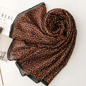 Dettaglio del motivo paisley sulla lunga sciarpa di seta con accenti arancio e neri