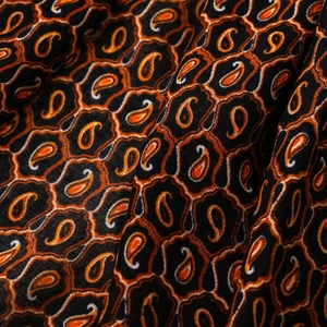 Dettaglio macro del tessuto a motivo paisley nero e arancione per sciarpe e scialli
