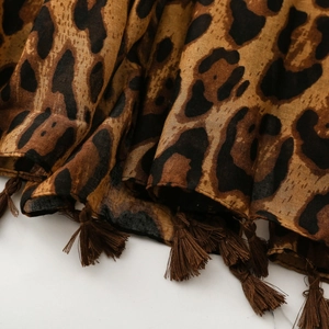 Detailed close-up of leopard print chiffon scarf fabric with brown fringed tassel edges