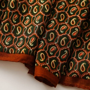 Macro del tessuto con motivo paisley e dettagli floreali bohémien in verde scuro e arancio