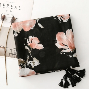 Détail d'écharpe noire au toucher lin avec motifs floraux roses et pompons élégants