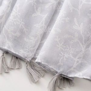 Close-up of lightweight Bali yarn scarf featuring white floral embroidery and tassel fringe